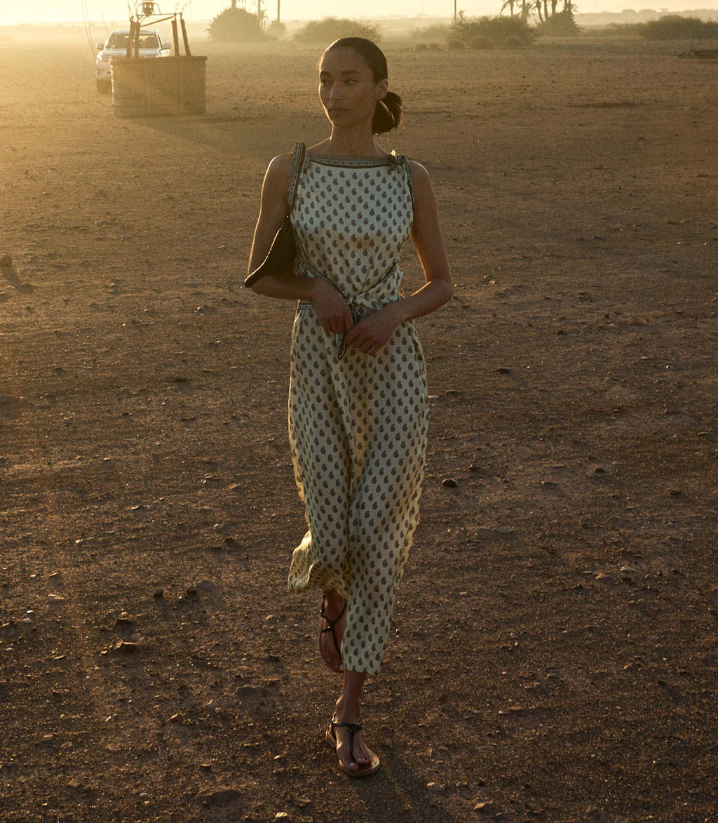 Woman in a paisley dress standing in a desert landscape with a sunset.