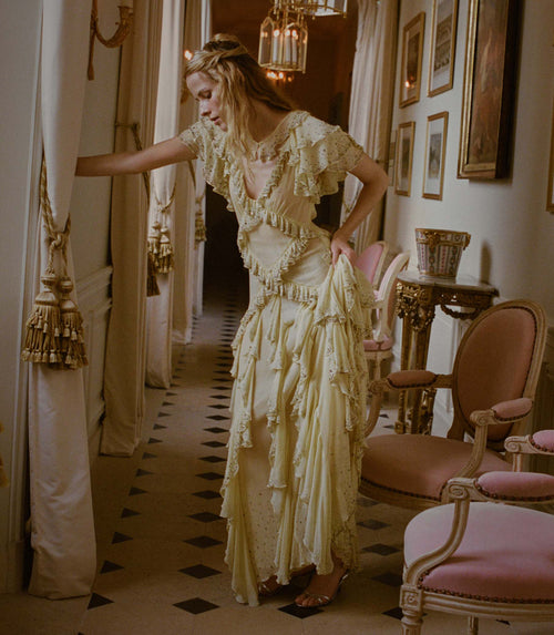 Woman in a vintage-style yellow dress standing in an elegant room with ornate decor.