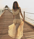 Woman in a cream lace dress walking on a wooden pier by the water.