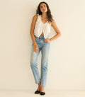 Woman wearing a white sleeveless top and light blue jeans against a plain background