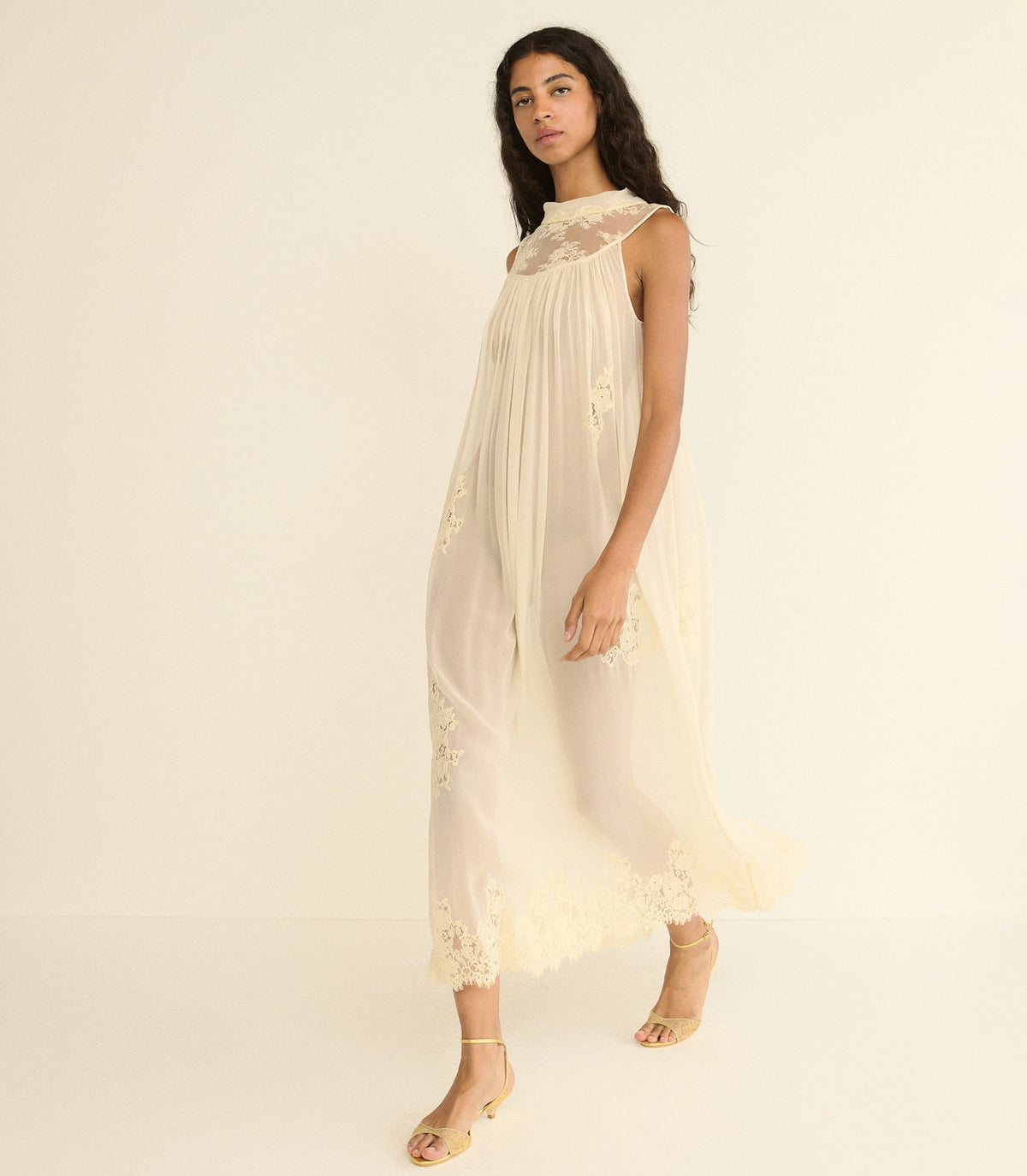 Woman wearing a off white lace dress against a plain background