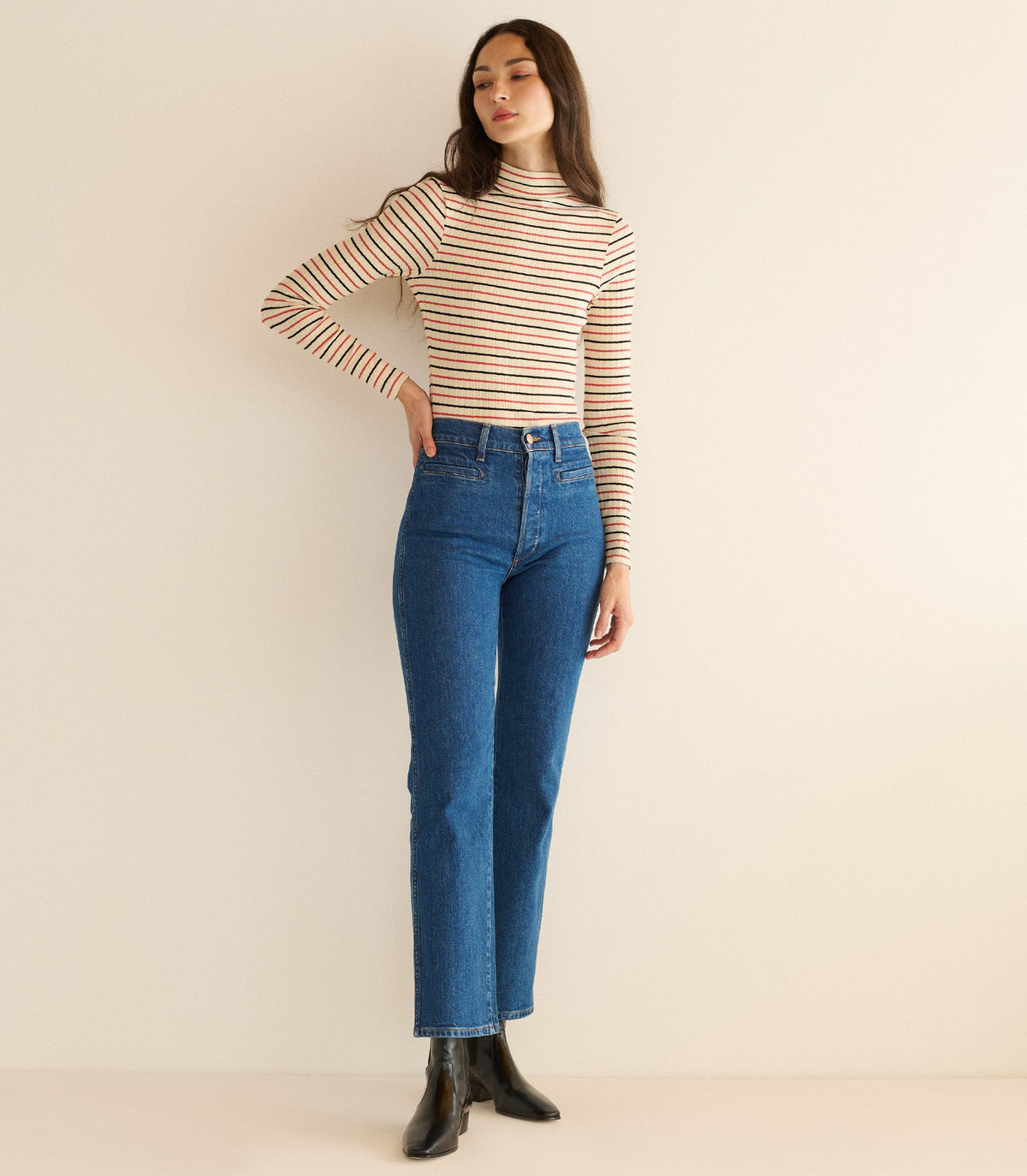 Woman wearing a striped long-sleeve top and blue jeans against a beige background