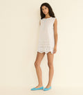 Woman wearing a white sleeveless dress with lace details on a beige background