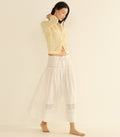 Woman wearing a yellow textured cardigan and white skirt on a beige background