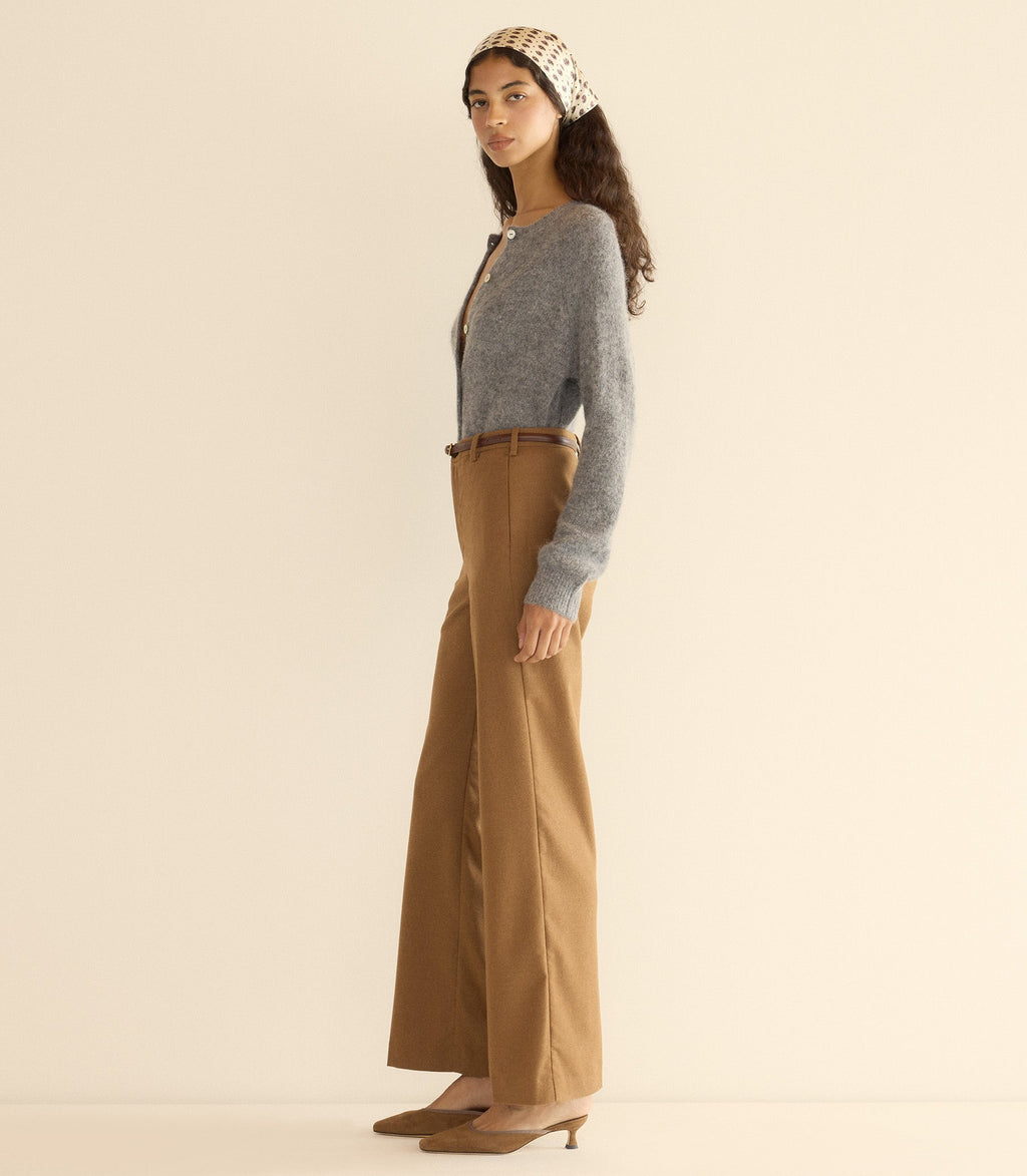 Woman wearing a gray cardigan and brown pants with a beige headband against a plain background