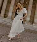 Woman in a white pin dot dress standing in front of classical architecture